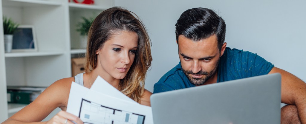 Young couple looking at blueprints and a computer to find the best rate for a mortgage
