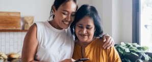 Two women hugging and smiling, whilst looking at a mobile phone