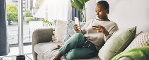 Shot of a young woman using her card and phone to shop online at home