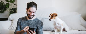 Man with laptop using mobile phone while sitting by dog at home