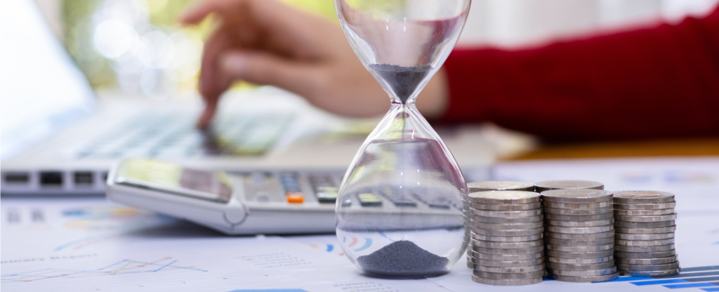 Person on laptop, with some coins and an hourglass.